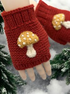 Knitted mushroom-themed fingerless gloves styled with autumn leaves and natural woodland elements."