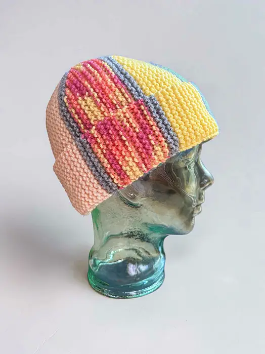 Free knit flat beanie pattern using leftover yarn on a glass display head