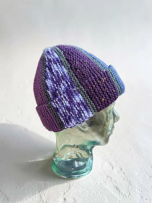 Colourful mosaic knit cap made from scrap yarn on a glass mannequin head