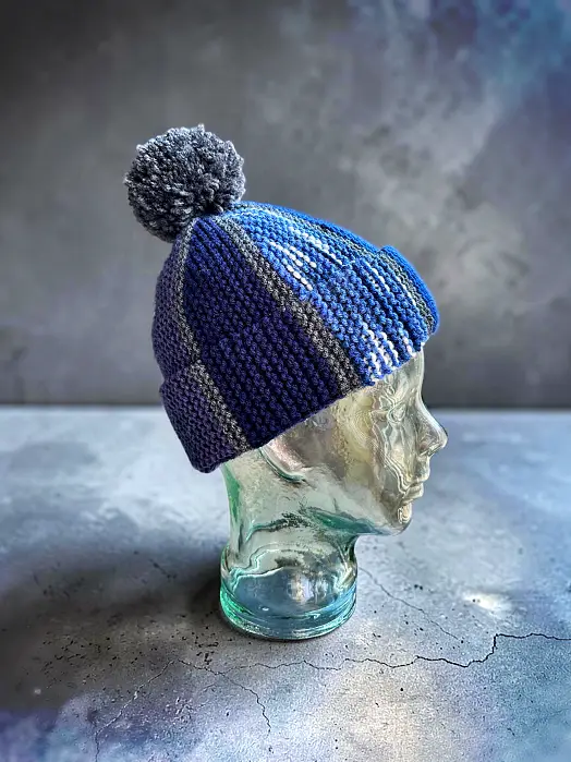 Knit winter hat made with leftover yarn displayed on a glass head, free knitting pattern